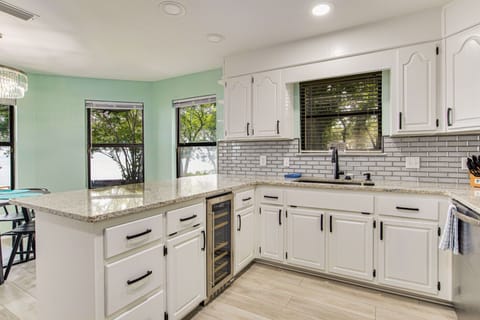 Modern kitchen with white cabinetry granite counters and wine cooler at Gulf Breeze bayfront house near Pensacola