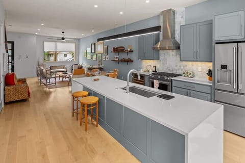 Modern open-concept kitchen and living area with soft blue cabinets, a sleek island, and warm natural wood flooring.