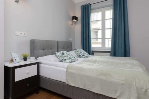 A cozy bed with soft green and white bedding is set near a window adorned with elegant blue curtains, creating a peaceful ambiance.