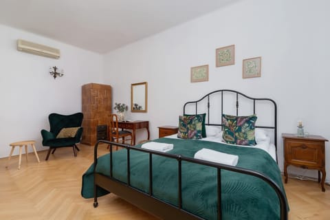 A stylish bedroom with a decorative wrought iron bed, green bedding, and vintage furniture.

