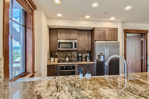 A modern kitchen featuring stainless steel appliances, wooden cabinets, a granite countertop, and a window with a view.