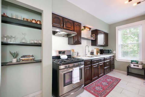 Cook in style with sleek appliances, rich wood cabinets, and open shelving. Thoughtful details like glassware, cookbooks, and a cozy rug add character to this bright, welcoming space!