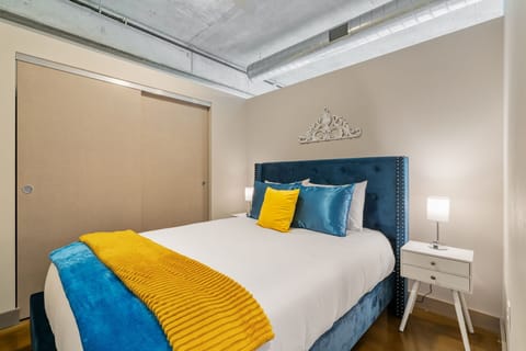 Sink into plush bedding with vibrant blue and yellow accents in your stylish bedroom featuring industrial-chic exposed ceilings.
