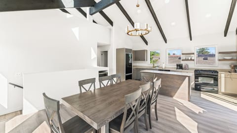 - Bright dining and kitchen area with open concept style  
- Wooden table with seating for group meals together  
- Modern chandelier and vaulted ceilings with beams