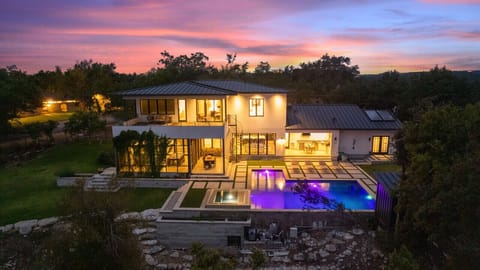 A stunning sunset view showcasing the home’s modern design, glowing interiors, and illuminated pool, all set against a peaceful natural backdrop.