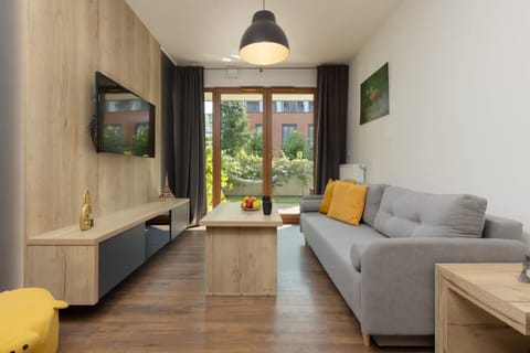 Modern living room with a grey sofa, a coffee table, and access to a garden-view balcony.

