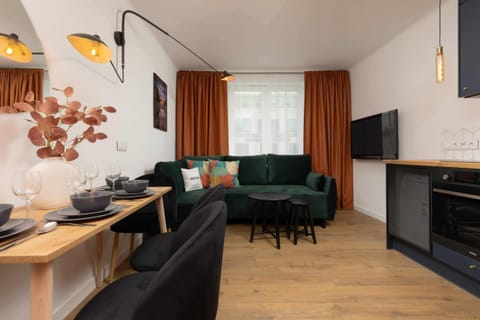 A cozy living and dining area with a green sofa, orange accents, and modern lighting.

