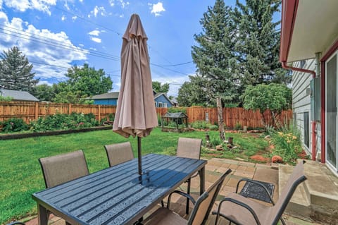 Outdoor dining table with umbrella opens to a green backyard framed by fencing and trees, inviting slow lunches, morning coffee, or relaxed conversations while enjoying fresh air and open sky right outside the door.