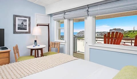 Relax in bed while watching waves through wide sunny windows.
