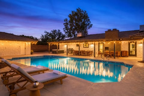 Resort-style backyard with sparkling pool, loungers, and lit patio dining