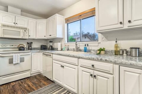 Bright white kitchen with long counters, upper cabinets, and a window over the sink—plenty of room to prep ingredients, cook a favorite meal, and keep everything within easy reach.