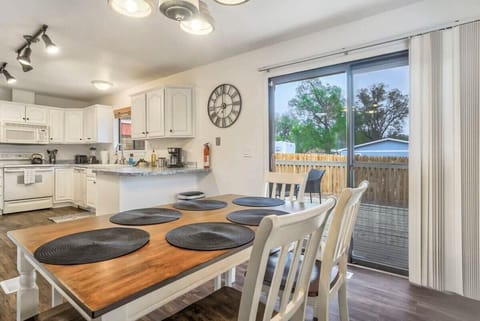 Wooden dining table set with round placemats beside a bright kitchen and sliding glass door—pull up a chair for slow breakfasts, shared meals, or planning the day with natural light pouring in.