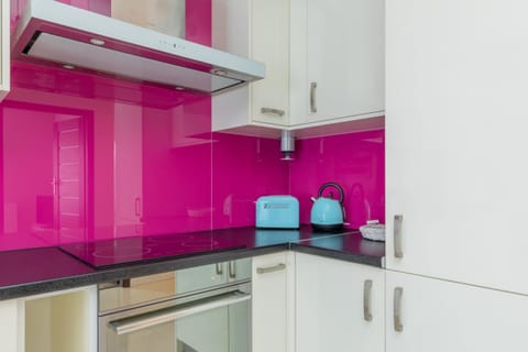 A contemporary kitchen with white cabinetry, high-gloss pink backsplash, and state-of-the-art appliances for a functional yet stylish look.