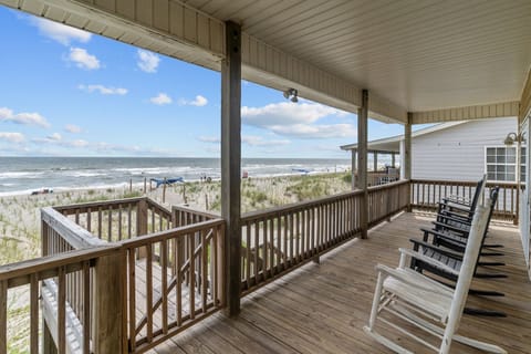 Covered oceanfront deck with rocking chairs, wood railings, dune views, and direct sightlines to the beach and rolling Atlantic waves.