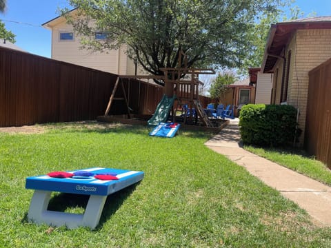 Fully enclosed back yard with a fire pit, grill, chairs, play set and corn hole.