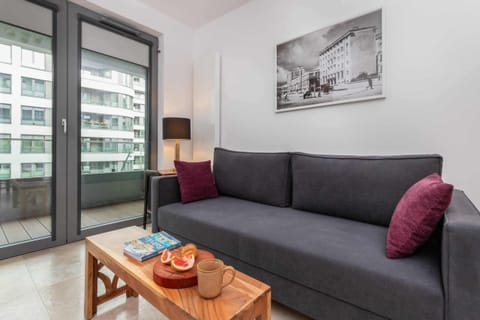 A cozy living room featuring a modern gray sofa, vibrant red cushions, and a wooden coffee table, complemented by a large window for natural light.

