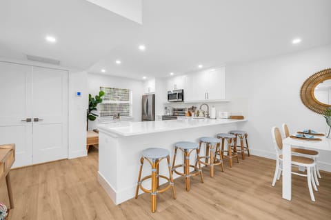 There are 5 sky-blue rattan bar stools at the impressively large quartz kitchen counter. The kitchen also has a kitchen nook with 2 upholstered rattan and cane benches, a modern contemporary white round table, and a decorative Fiddle tree.