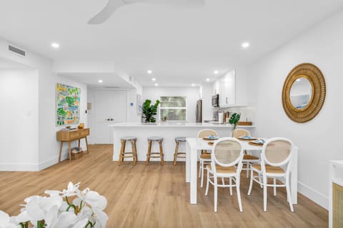 There are 5 sky-blue rattan bar stools at the impressively large quartz kitchen counter. The kitchen also has a kitchen nook with 2 upholstered rattan and cane benches, a modern contemporary white round table, and a decorative Fiddle tree