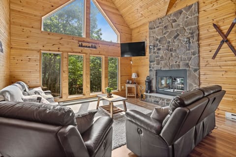 This sunlit living room boasts soaring ceilings, warm wooden accents, and a stunning stone fireplace. Sink into the plush leather seating and enjoy breathtaking forest views through the expansive windows.