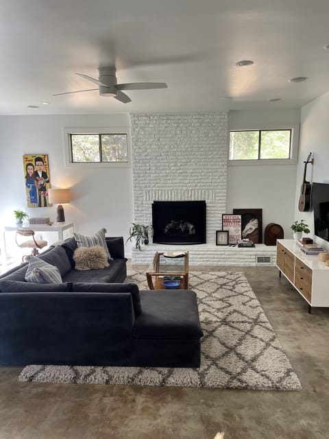 Large sunlit sunken den with sectional seating, 65" smart TV, and desk. 
