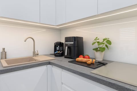 A modern kitchenette with sleek white cabinets, a coffee machine, and all essential appliances.

