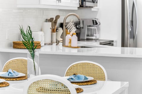 The modern white table seats 4 for intimate dining, There are 4 natural cane dining chairs to add to that coastal flair and an impressively large round rattan "sun" mirror that centers over the dining table.