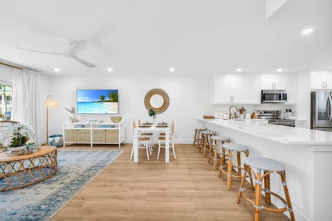 The modern white table seats 4 for intimate dining, There are 4 natural cane dining chairs to add to that coastal flair and an impressively large round rattan "sun" mirror that centers over the dining table.