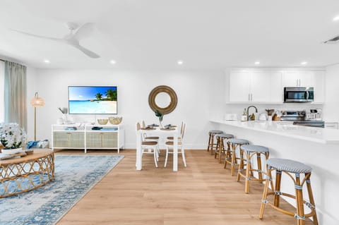 The modern white table seats 4 for intimate dining, There are 4 natural cane dining chairs to add to that coastal flair and an impressively large round rattan "sun" mirror that centers over the dining table.