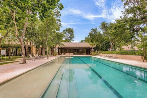 Enjoy a refreshing swim in the spacious outdoor pool, surrounded by lush greenery and loungers.