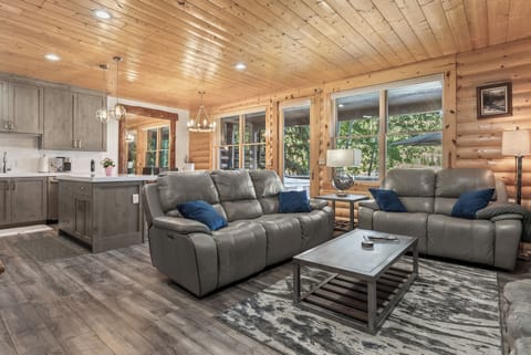 - Open concept living room with cabin wood accents and leather sofas  
- Large windows bring natural light and peaceful forest views inside  
- Relax in comfort after outdoor adventures in the mountains