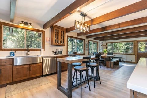 The open kitchen features a full range of stainless steel appliances, spacious countertops, a wine fridge, and big windows with views over the surrounding trees.