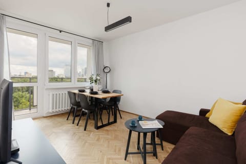 A spacious dining and living area with a wooden table, black chairs, and a comfortable brown sofa with yellow pillows.

