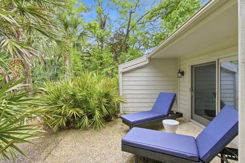 Sapphire cushions rest against a quiet patio, offering a private corner to soak in the afternoon glow. Vibrant palms and towering oaks create a lush screen of emerald green, wrapping this secluded outdoor nook in natural peace.