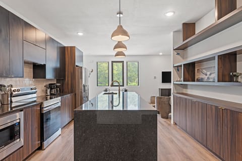 Sleek, modern kitchen with stainless steel appliances, a large island, and pendant lighting—perfect for cooking, gathering, or enjoying meals during your stay in walkable Downtown Shawnee.
