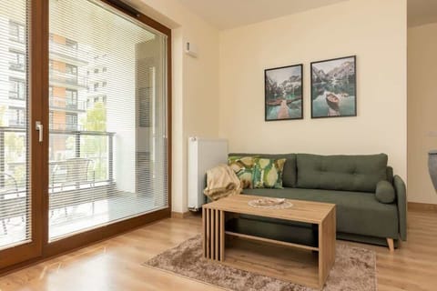A cozy living room with a comfortable green sofa, a coffee table, and large windows providing natural light.
