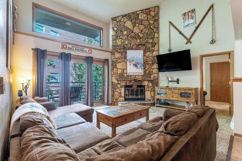 Living room with vaulted ceilings, floor-to-ceiling stone wood-burning fireplace, flatscreen Smart TV, and games.
