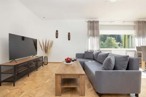 Bright living area with a large, comfortable sofa, wooden coffee table, and a flat-screen TV, offering plenty of natural light.

