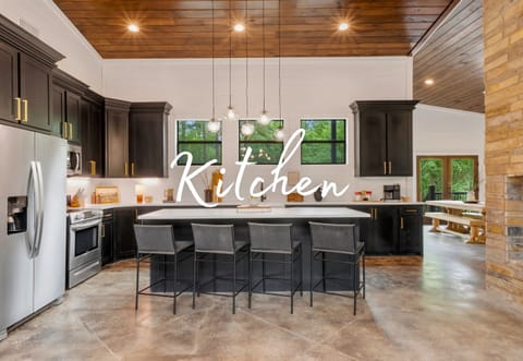 Cook in style in this sleek, modern kitchen featuring dark cabinetry and gold accents, all while being part of the conversation at the spacious island.