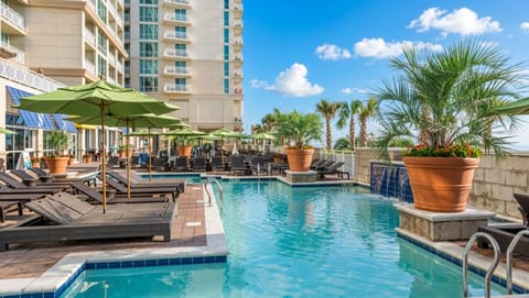 Outdoor Pool • Resort Towers, Green Umbrellas & Palm Planters