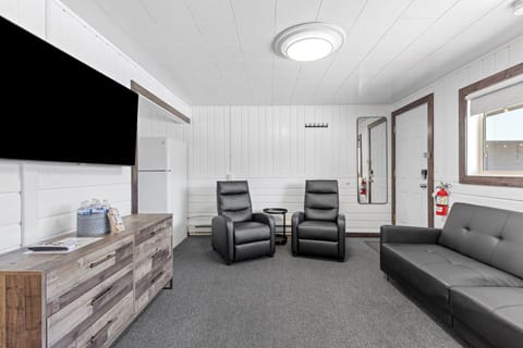 Living room with pull out sofa bed, two reclining chairs, flat screen Tv and access to kitchen