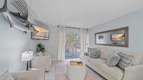 A modern living room with a neutral color palette, comfy sofas, a mounted TV, and sliding doors to the patio.