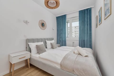 A cozy bedroom featuring a comfortable bed, soft white bedding, and a blue curtain, creating a relaxing ambiance.
