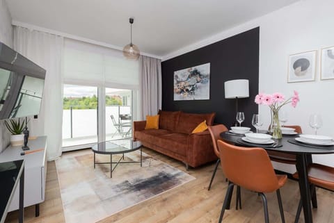 A stylish living and dining area with a brown sofa, orange dining chairs, and a black accent wall, creating a cozy and modern atmosphere.

