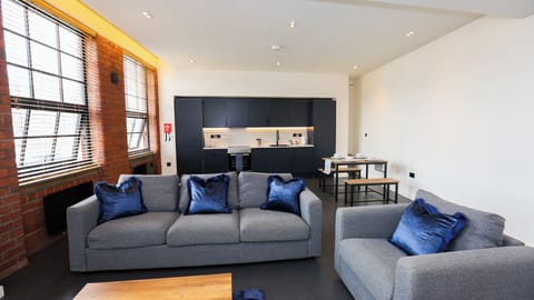 Bright living area with twin grey sofas, blue scatter cushions, exposed brick walls and dining table – The Nichols Bldg, Sheffield