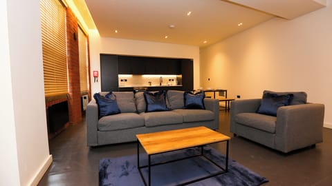 Lounge with exposed red brick, twin grey sofas and TV unit, large industrial window – The Nichols Bldg, Sheffield