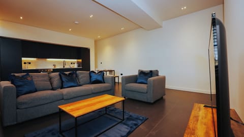 Open-plan lounge and kitchen with wood coffee table, blue accent cushions, and ambient lighting – The Nichols Bldg, Sheffield