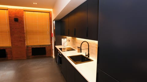 Contemporary kitchen with black cabinets, integrated oven, sink, red brick feature wall – The Nichols Bldg, Sheffield