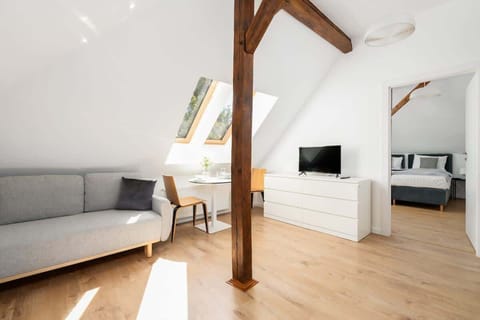 A bright attic living area featuring wooden beams, a cozy sofa, and a TV, with natural light streaming in from skylights.

