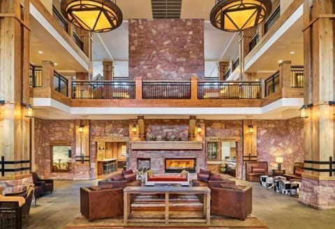The grand lobby, featuring soaring ceilings and rich wooden accents, invites guests to unwind by the stunning stone fireplace, blending rustic charm with upscale comfort.