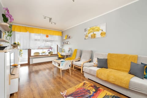 A bright and cozy living room with yellow accents, a comfortable sofa, a stylish coffee table, and large windows letting in natural light.